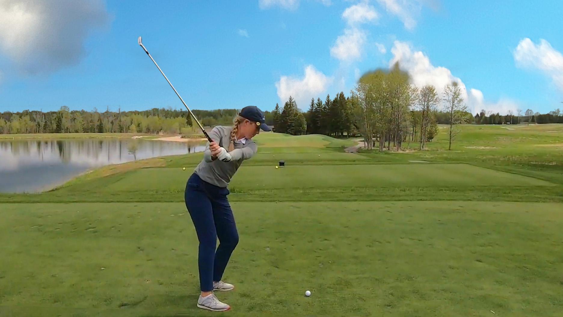 A woman swinging a golf club at a course in Escanaba