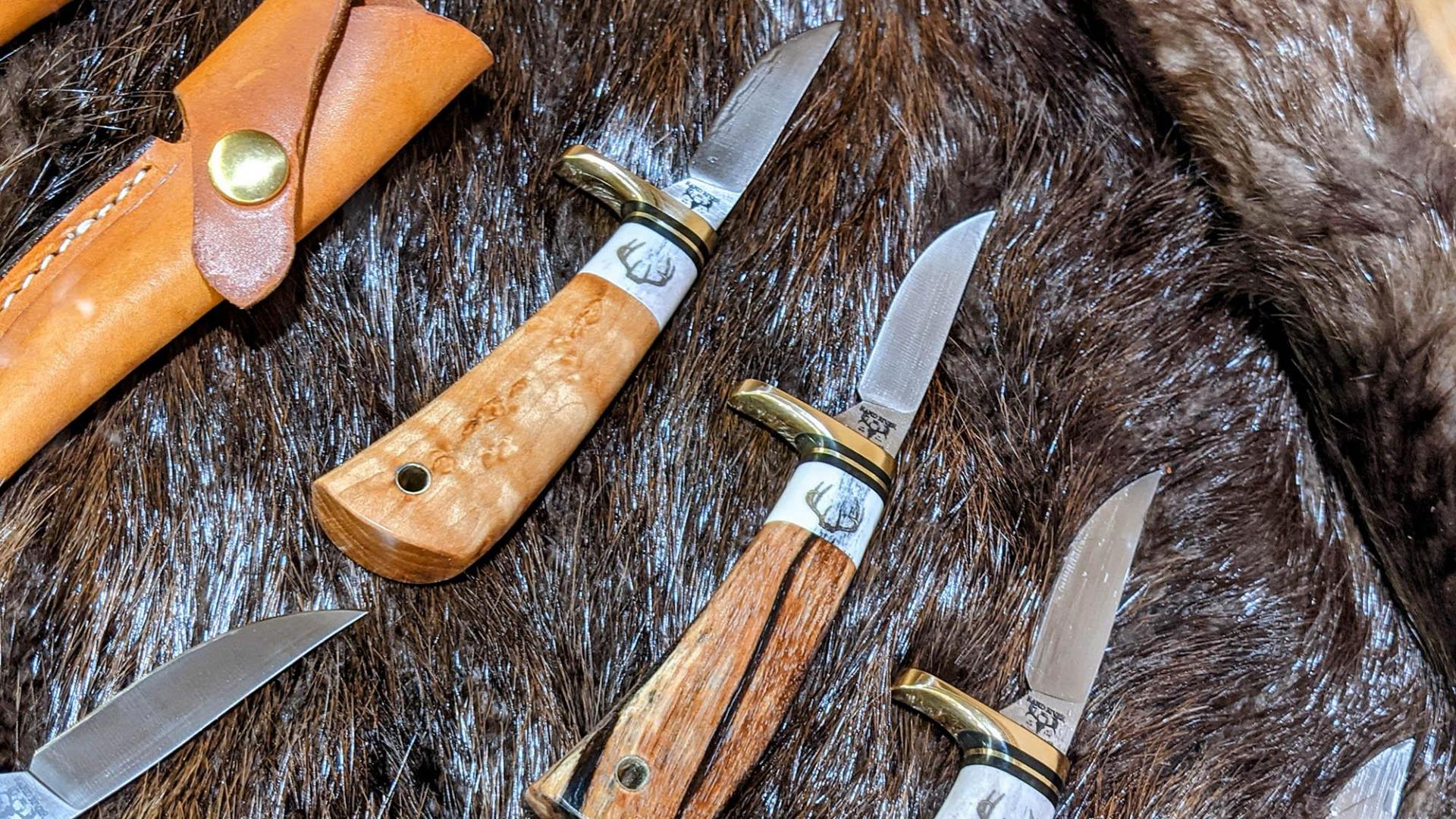 A row of knives on a fur blanket at Rapid River Knifeworks