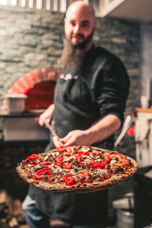 Cook holding out a freshly cooked pizza