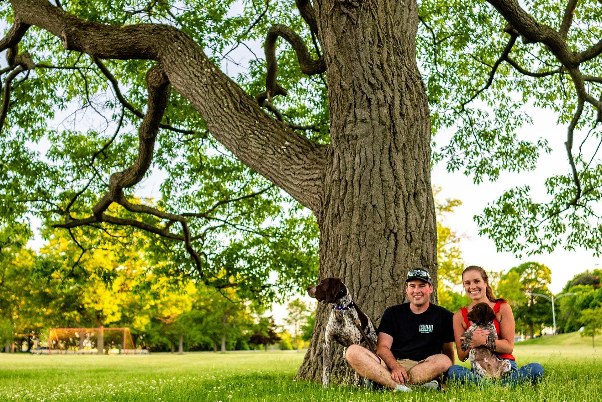 People sitting near a tree with a dog.