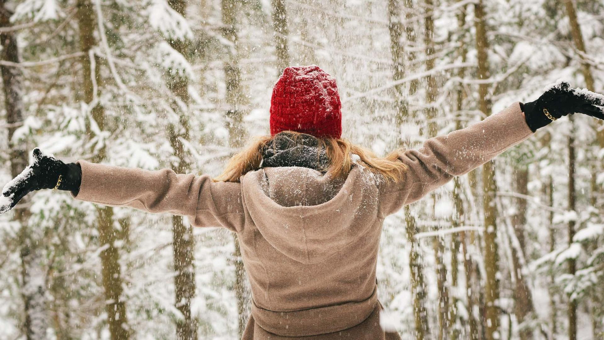 A person enjoying the falling snow while hiking in the woods.