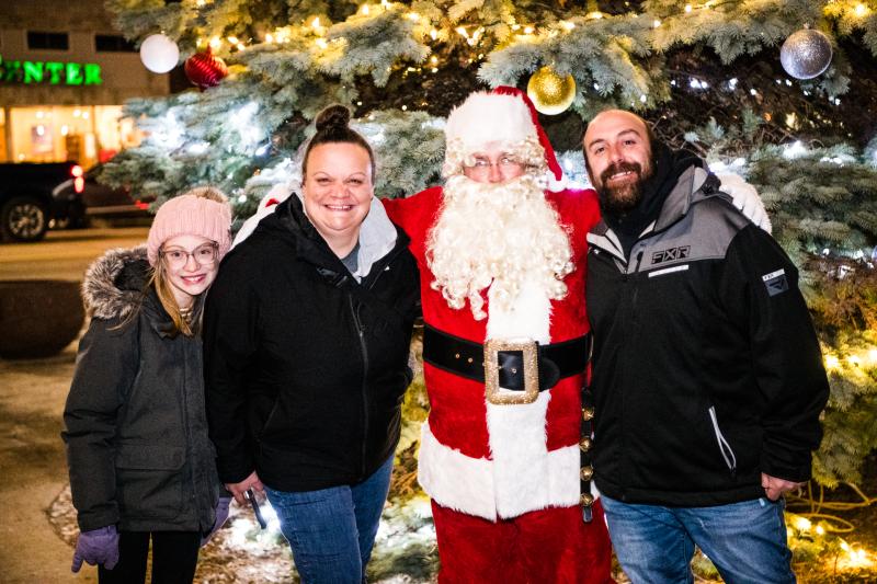 A family posing for a photo with Santa by a Christmas tree.