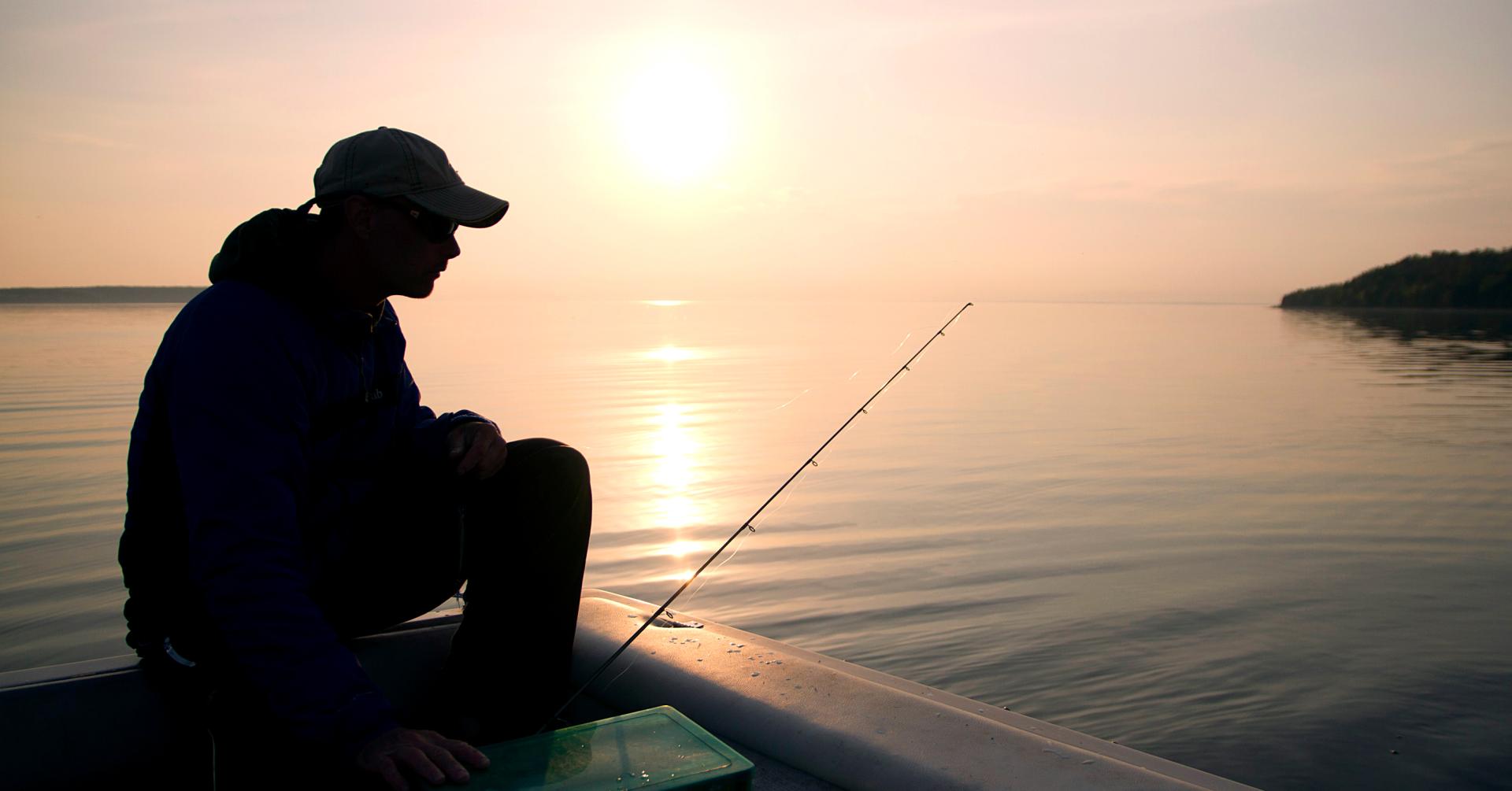 A fisherman sitting in a boat at sunrise.