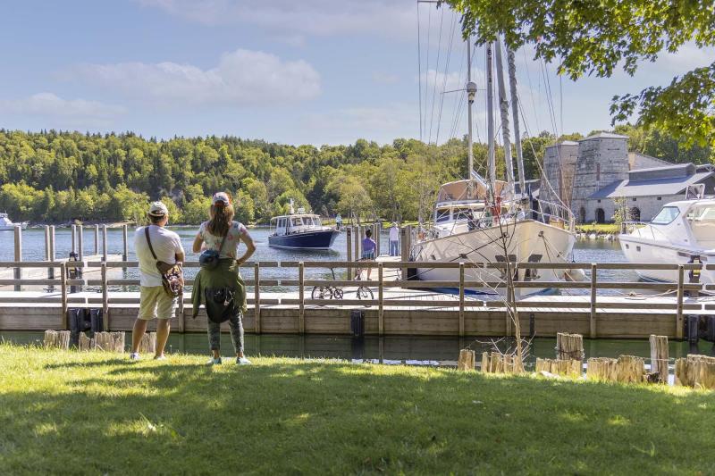 Two people look out over Snail Shell Harbor, where boats are moored and historic buildings stand along the opposite shore.