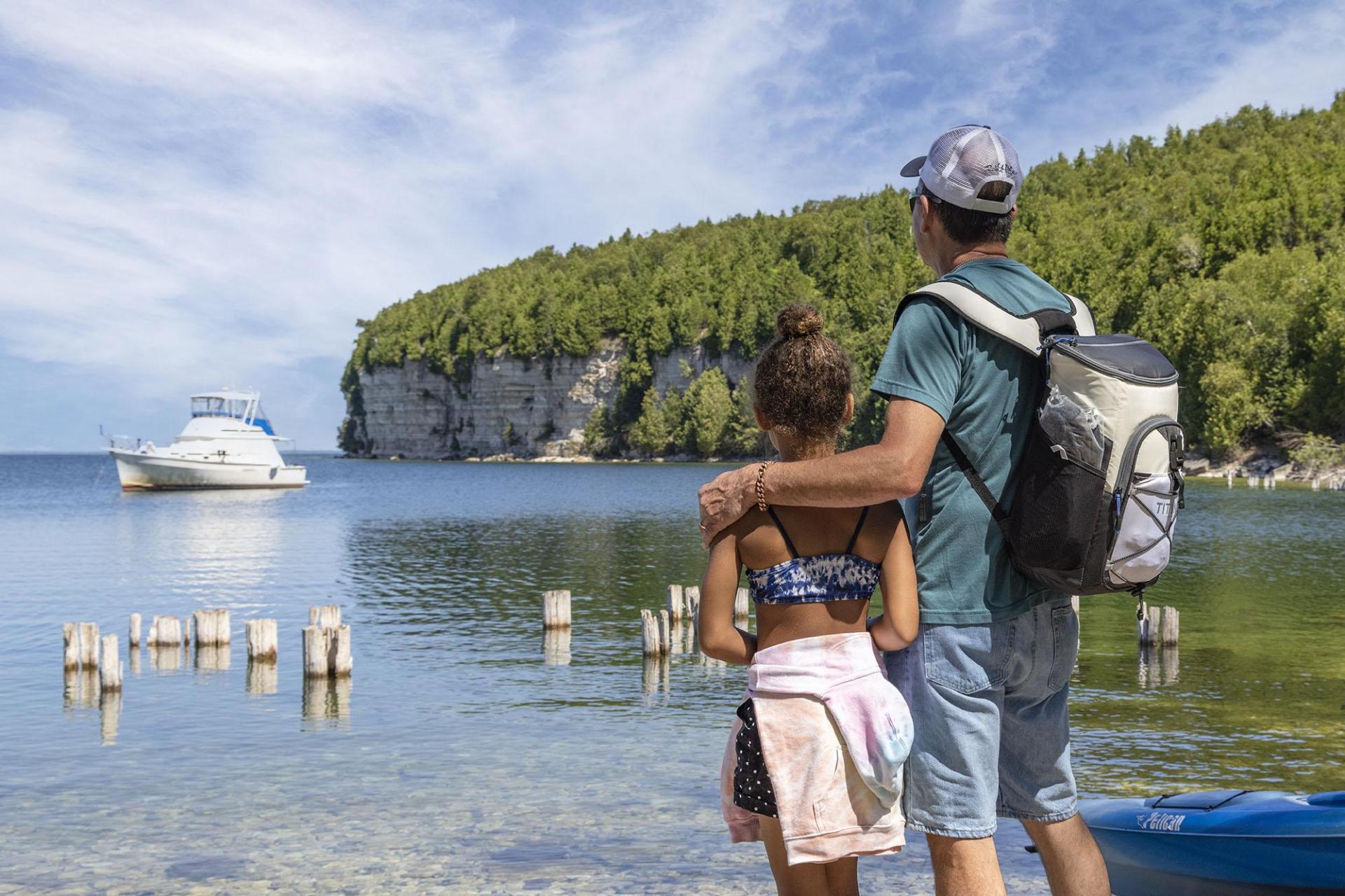 A grandfather and granddaughter look out across Snail Shell Harbor toward the cliffs..