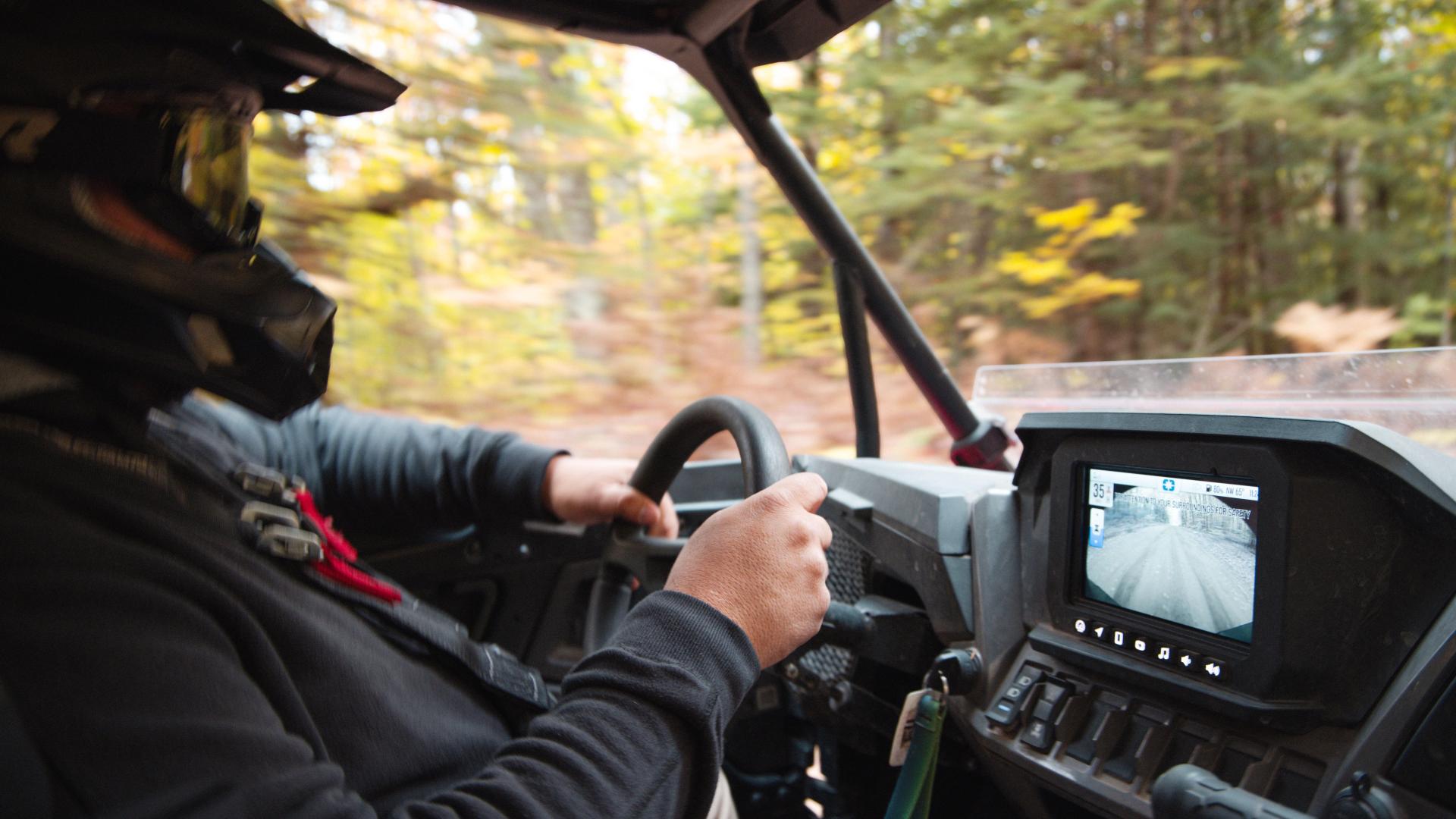 A side-by-side traveling along a forest road in early fall, with hints of changing foliage.