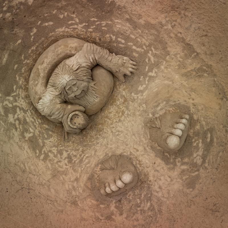 An aerial view of a sand sculpture depicting Bigfoot relaxing in an inflatable tube.
