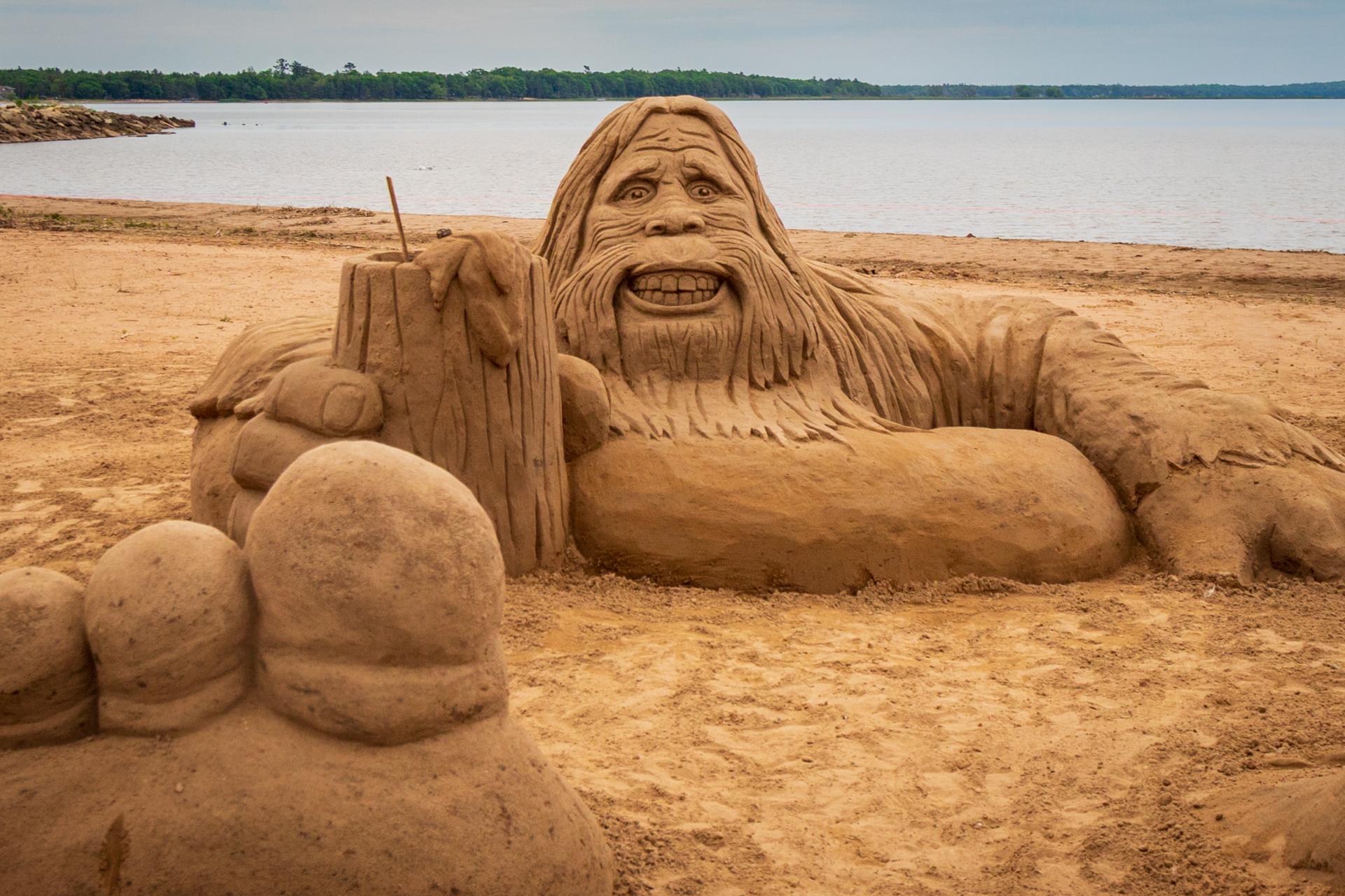 An aerial view of a sand sculpture depicting Bigfoot relaxing in an inflatable tube.