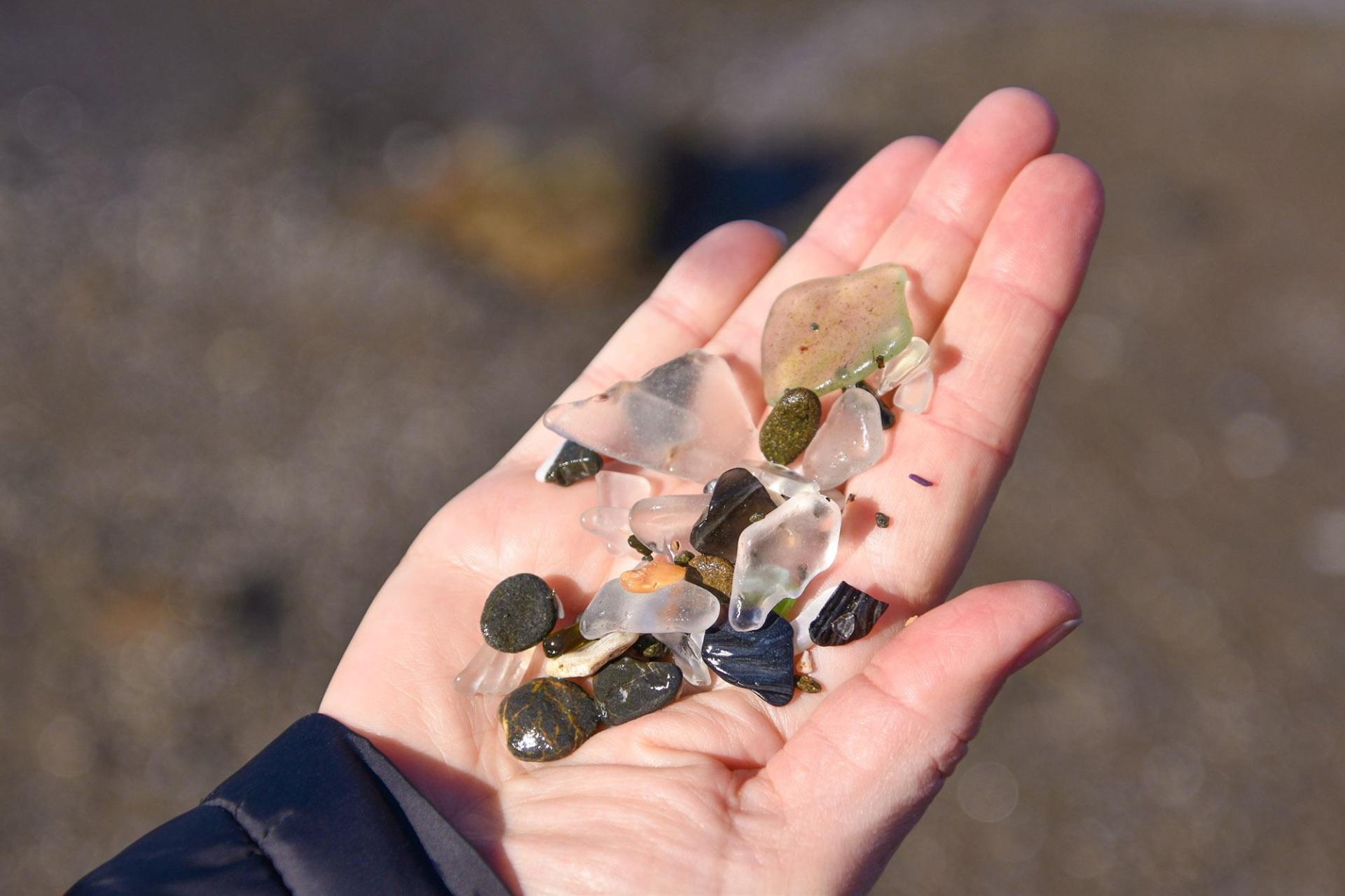 A person holding a handful of beach glass and small stones.