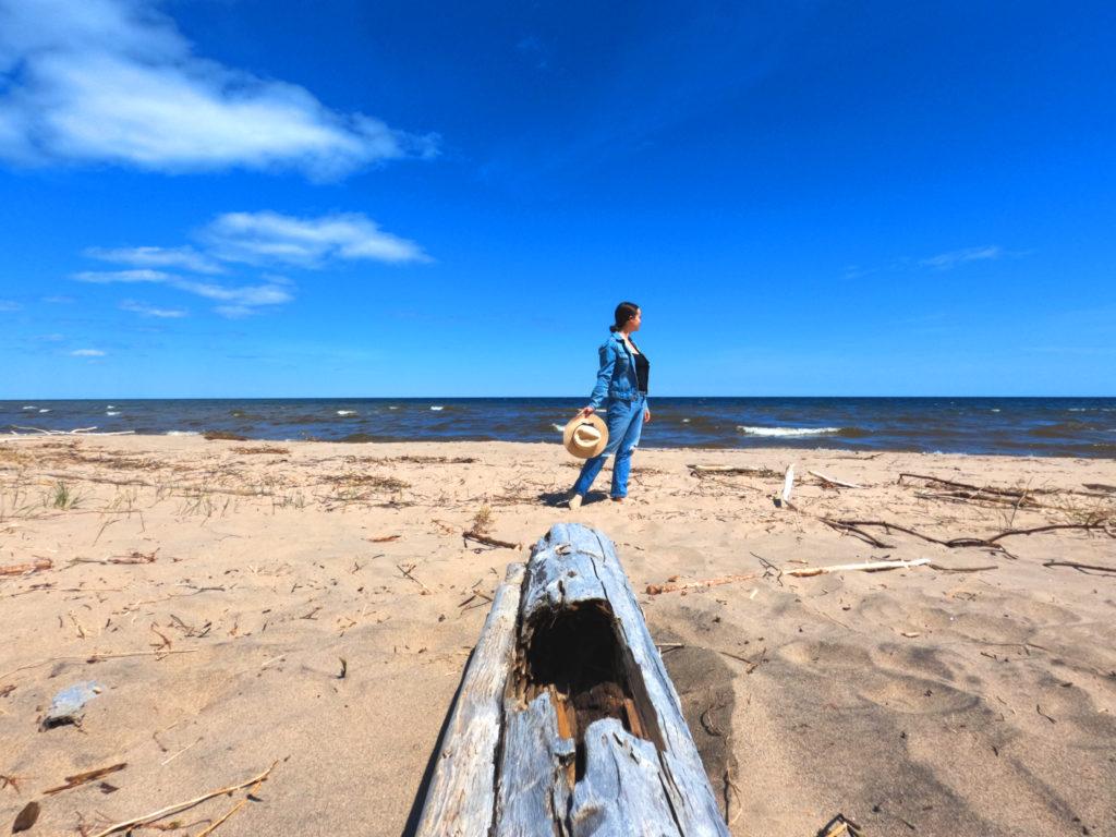 woman standing on beach amidst driftwood