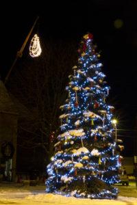 a lit-up pasty hanging in the air next to a lit Christmas tree (at night)