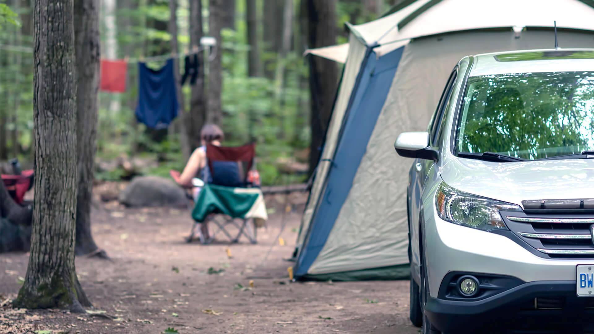 woman sitting on camp chair in a campsite with tent and car