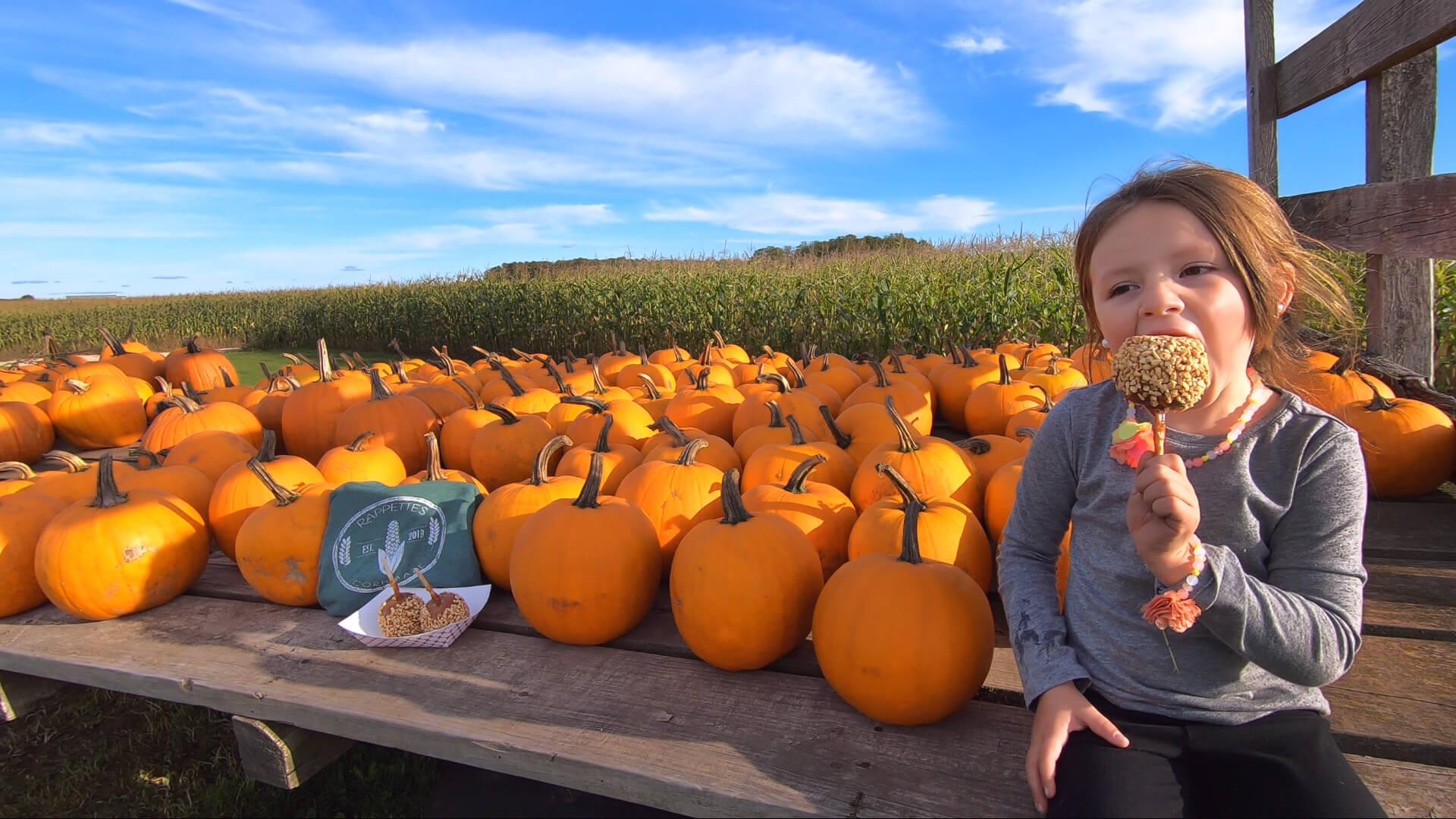 girl eating caramel apple near a patch of pumpkins