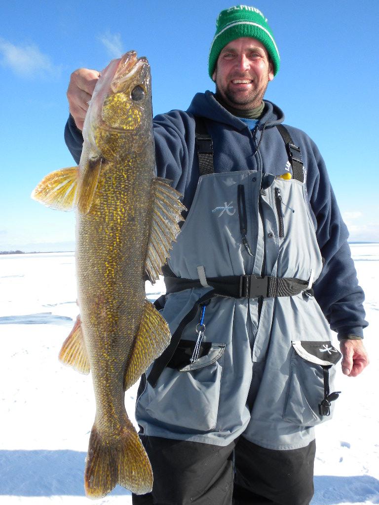Man holding up his freshly caught walleye on the icy lake.