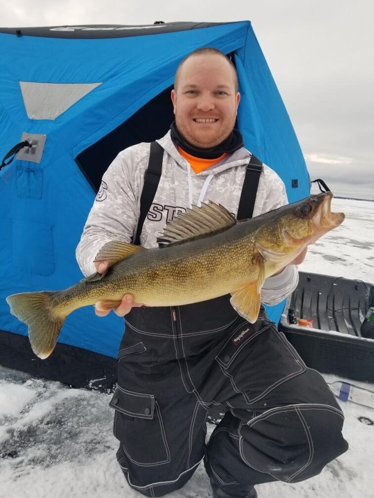Man holding up his trophy fish inside his ice fishing shanty.